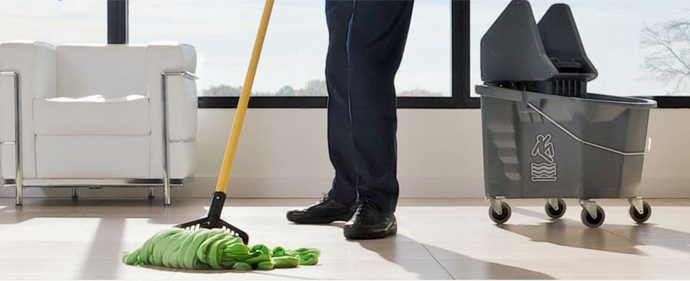 Cleaning professional mopping a modern floor with a green mop and bucket.